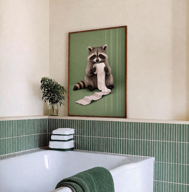 May include: A framed print featuring a raccoon holding a roll of toilet paper against a green background. The artwork has a brown frame and is displayed in a bathroom setting with green and white accents. The raccoon is depicted in a realistic style.