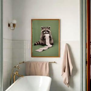 May include: A framed print featuring a raccoon holding a roll of toilet paper against a green background. The raccoon is depicted in shades of gray and brown, with a black mask and striped tail. The frame is a warm wood tone.