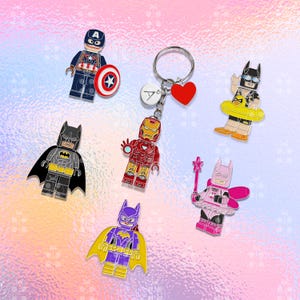 Puede incluir: Colecci&oacute;n de llaveros con tem&aacute;tica de superh&eacute;roes. Incluye al Capit&aacute;n Am&eacute;rica con escudo, Batman, Iron Man y otros personajes. Los llaveros son coloridos y presentan un dije de coraz&oacute;n y un dije con una letra.