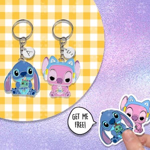 Puede incluir: Dos llaveros con personajes de dibujos animados, uno azul y otro rosa, cada uno con un llavero plateado y un peque&ntilde;o dije. El personaje azul sostiene una peque&ntilde;a mu&ntilde;eca verde. El personaje rosa lleva auriculares. Una pegatina dice "GET ME FREE!"