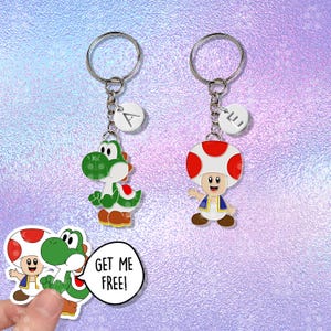 Puede incluir: Dos llaveros con los personajes de dibujos animados Yoshi y Toad de la serie de videojuegos Super Mario. El llavero de Yoshi es verde y blanco, y el llavero de Toad tiene una gorra de hongo roja y blanca. Cada llavero tiene un anillo plateado y un dije blanco con una letra.