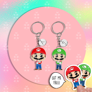 Puede incluir: Dos llaveros con los personajes de dibujos animados Mario y Luigi, cada uno con un llavero plateado y un peque&ntilde;o dije inicial. Mario lleva un gorro rojo y Luigi uno verde. La frase "GET ME FREE!" est&aacute; en un bocadillo.