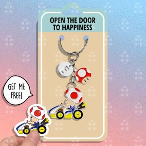 May include: A novelty keychain with a mushroom character in a blue and yellow kart. The keychain has a mushroom charm and a charm with the letter "E". The packaging reads "OPEN THE DOOR TO HAPPINESS".
