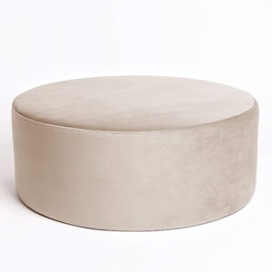 May include: A round, light beige ottoman with a soft, plush fabric covering.