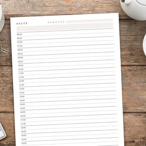 May include: A daily planner sheet with the word "HEUTE" at the top, featuring time slots from 6:00 to 20:00. The planner is on a wooden surface, alongside a cup of tea, a teapot, a pen, and a keyboard.