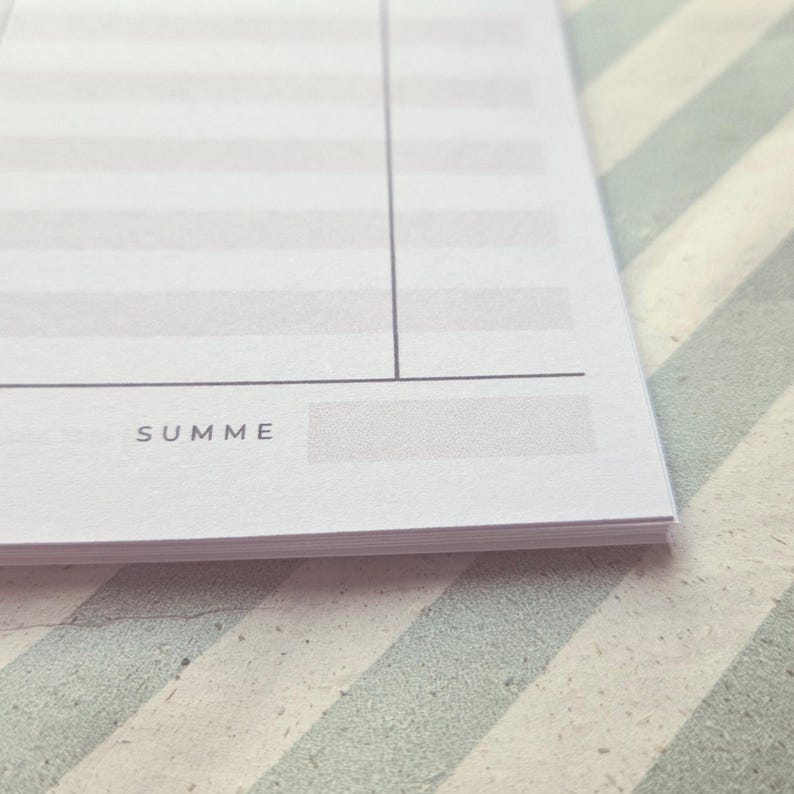 May include: A white notepad with light gray horizontal stripes and a vertical line. The bottom left corner features the word SUMME printed in dark gray, followed by a rectangular gray box for writing, all on a stack of paper sheets.