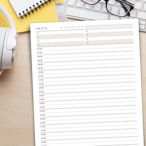May include: A white paper planner with the word "HEUTE" at the top, featuring a schedule layout with time slots from 7:00 to 19:00. The planner is on a light wood surface, with a keyboard, glasses, and headphones in the background.