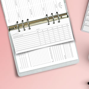 Könnte beinhalten: Offener Planer mit einer Gewohnheitstracker-Seite, die ein Wochenlayout mit Kreisen zur Markierung des täglichen Fortschritts aufweist. Der Planer liegt offen auf einer rosa Oberfläche, mit einer Tastatur und einer Tasse Kaffee in der Nähe.