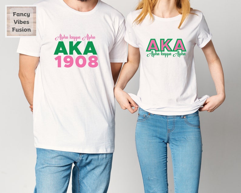 May include: Two white t-shirts with the letters AKA in pink and green. The larger shirt has the text "Alpha kappa Alpha" and "1908" below the letters. The smaller shirt has the text "Alpha kappa Alpha" below the letters.