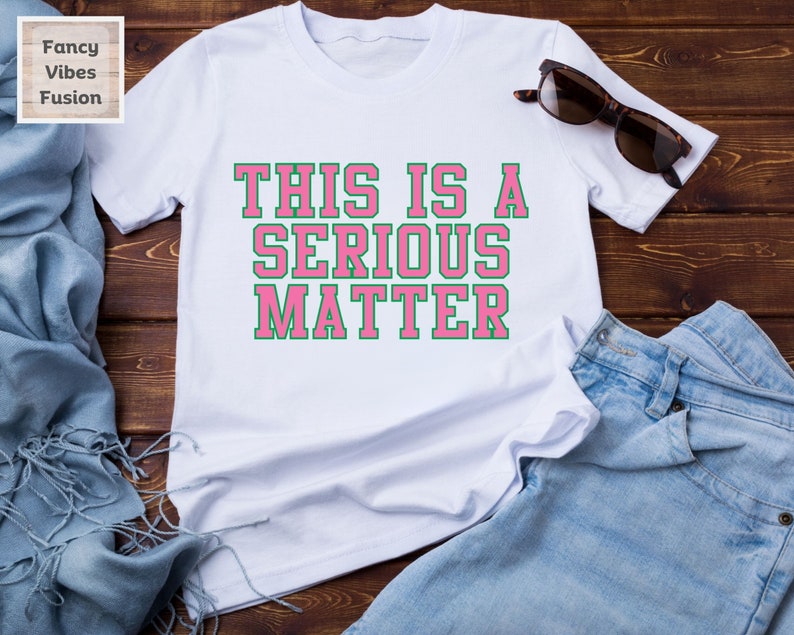 May include: White t-shirt with the text "THIS IS A SERIOUS MATTER" in pink letters with a green outline.