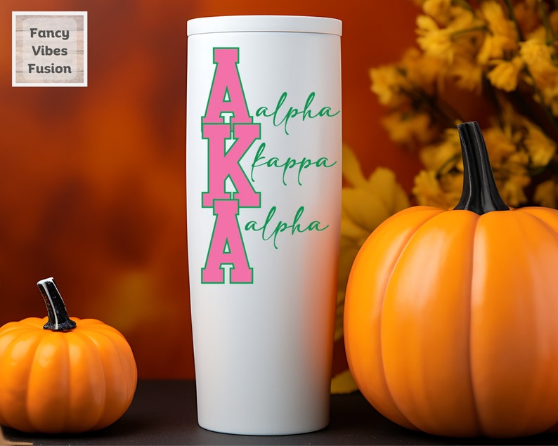 May include: White tumbler with a pink and green "AKA" design. The letters are outlined in green and the words "Alpha Kappa Alpha" are written in cursive green lettering.
