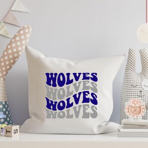May include: A white square cushion featuring the word "WOLVES" in a layered design of blue and grey text. The cushion is on a white shelf with decorative toys in the background.