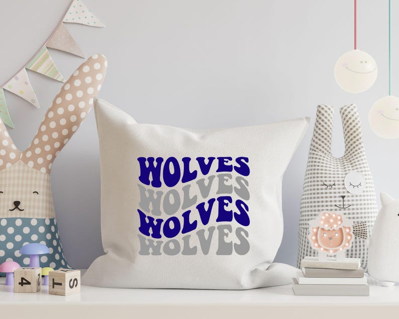 May include: A white square cushion featuring the word "WOLVES" in a layered design of blue and grey text. The cushion is on a white shelf with decorative toys in the background.