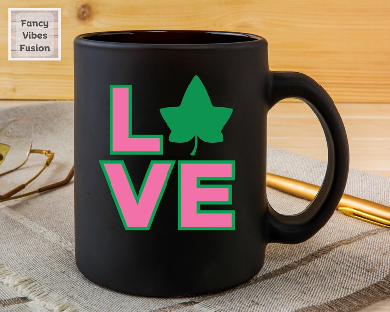 May include: Black ceramic coffee mug with a pink and green "LOVE" design featuring a green ivy leaf.