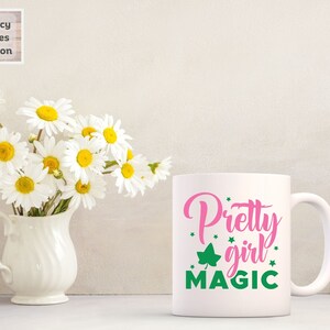 May include: White ceramic mug with a pink and green design. The text on the mug reads "Pretty girl magic".