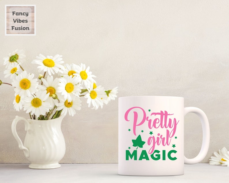 May include: White ceramic mug with a pink and green design. The text on the mug reads "Pretty girl magic".