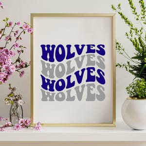 May include: A framed print featuring the word "WOLVES" in a layered, wavy design. The top and third instances of the word are in a deep blue, while the second and fourth are in grey. The frame is gold, and the background is white.