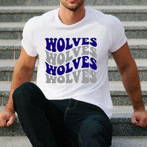 May include: White t-shirt featuring the word "WOLVES" in a repeating pattern. The word is in a wavy font, alternating between blue and grey. The shirt is short-sleeved and likely made of cotton.