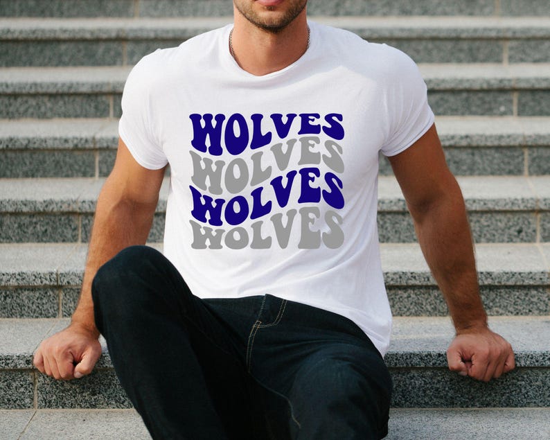 May include: White t-shirt featuring the word "WOLVES" in a repeating pattern. The word is in a wavy font, alternating between blue and grey. The shirt is short-sleeved and likely made of cotton.