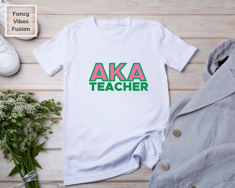 May include: White t-shirt with pink and green lettering that says "AKA TEACHER".