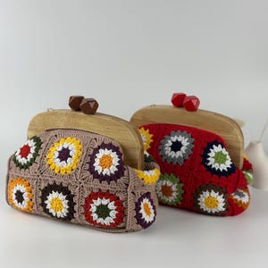 May include: Two crochet clutch bags with wooden frames. One is brown with colorful floral squares, the other is red with similar floral squares. The bags have wooden closures and are set against a white background.