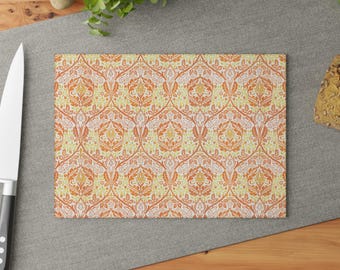 Peut inclure: Une planche à découper en verre avec un motif floral répété en orange, jaune et blanc. La planche est rectangulaire et a une surface lisse.