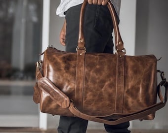 May include: A brown leather duffel bag with a long strap and gold hardware. The bag has a distressed look and is made of high-quality leather.