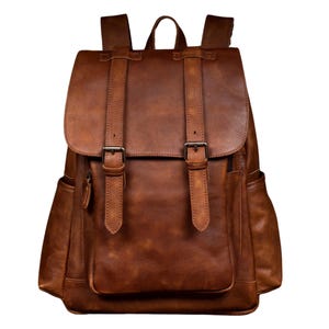 May include: A brown leather backpack with two adjustable straps and a front pocket. The backpack has a flap with two buckles.