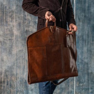 Travel-ready leather garment bag with a sleek design, perfect for hanging suits. Great for groomsmen, Christmas gifts, and as a durable accessory for men.
