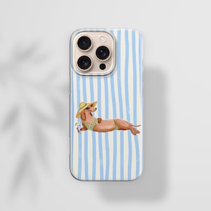 May include: A phone case with a light blue and white striped pattern. The case features an illustration of a dachshund wearing a sun hat and swimsuit, lounging with a drink. The phone case has a camera bump with three lenses.