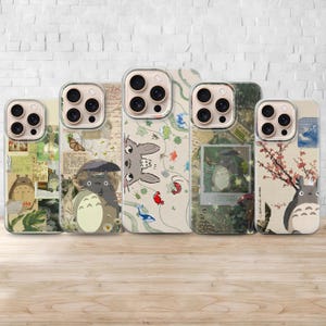 Puede incluir: Cinco fundas para teléfono con varios diseños con el personaje Totoro. Las fundas tienen bordes transparentes y están colocadas contra una pared de ladrillos blancos. Los diseños incluyen ilustraciones de Totoro, flores y otros elementos de inspiración japonesa.