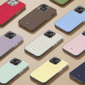 Può includere: Una collezione di custodie per telefoni colorate con un motivo a pois. Le custodie sono in vari colori, tra cui rosso, marrone, blu, viola, rosa, verde e giallo. Ogni custodia ha delle iniziali.