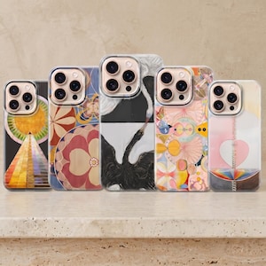 Op de afbeelding: Vijf smartphonehoesjes op een rij, elk met een eigen artistiek ontwerp. De hoesjes tonen patronen zoals een gouden zon boven een piramide, cirkelvormige bloemmotieven, twee vogels in zwart-wit, abstracte geometrische vormen en een hartvormig symbool.