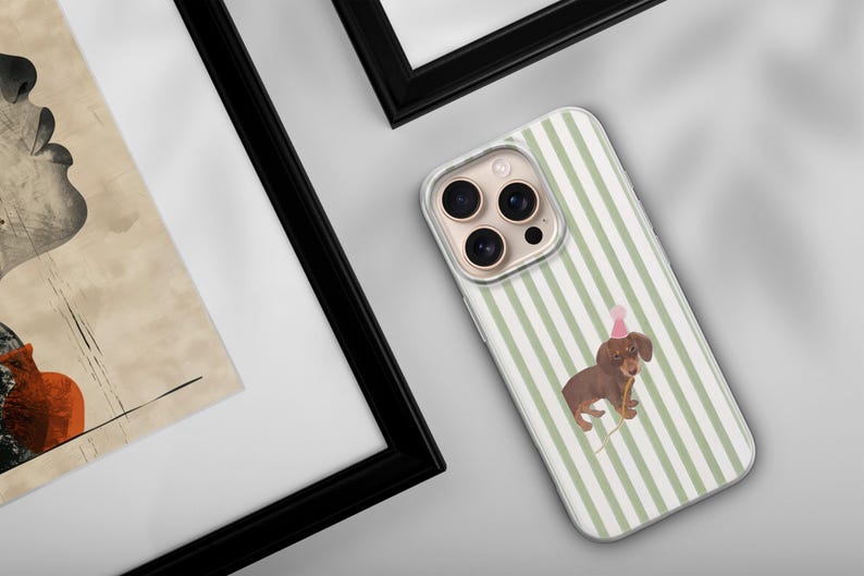 May include: A phone case with a green and white striped pattern. The case features a brown dachshund wearing a pink party hat and holding a party horn. The phone case is on a white surface.