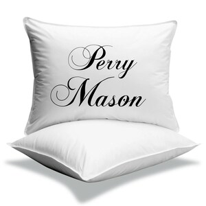 Pode incluir: Duas almofadas quadradas brancas empilhadas uma sobre a outra. A almofada superior tem as palavras "Perry Mason" impressas em elegante escrita preta. As almofadas s&atilde;o feitas de um material macio e liso.