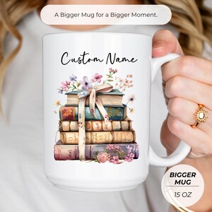 Puede incluir: Taza blanca de 444 ml con una ilustraci&oacute;n de una pila de libros y el texto "Custom Name". Los libros est&aacute;n decorados con flores y una cinta. La taza tambi&eacute;n tiene el texto "A Bigger Mug for a Bigger Moment."
