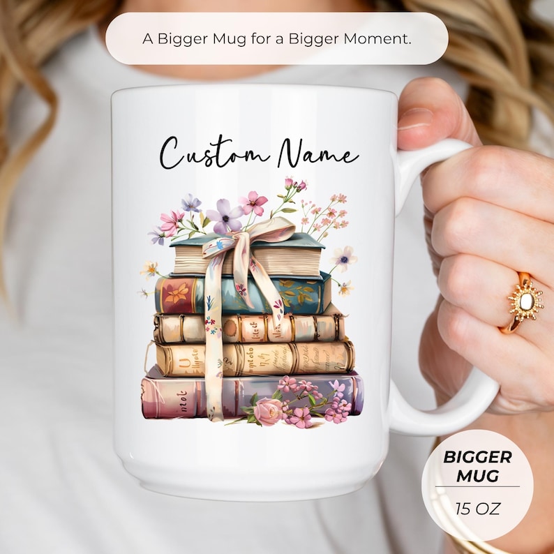 Puede incluir: Taza blanca de 444 ml con una ilustraci&oacute;n de una pila de libros y el texto "Custom Name". Los libros est&aacute;n decorados con flores y una cinta. La taza tambi&eacute;n tiene el texto "A Bigger Mug for a Bigger Moment."