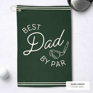 May include: Dark green golf towel with the text "BEST Dad BY PAR" in ivory script. A golf club and ball graphic is also featured. The towel has a metal grommet and a white border.