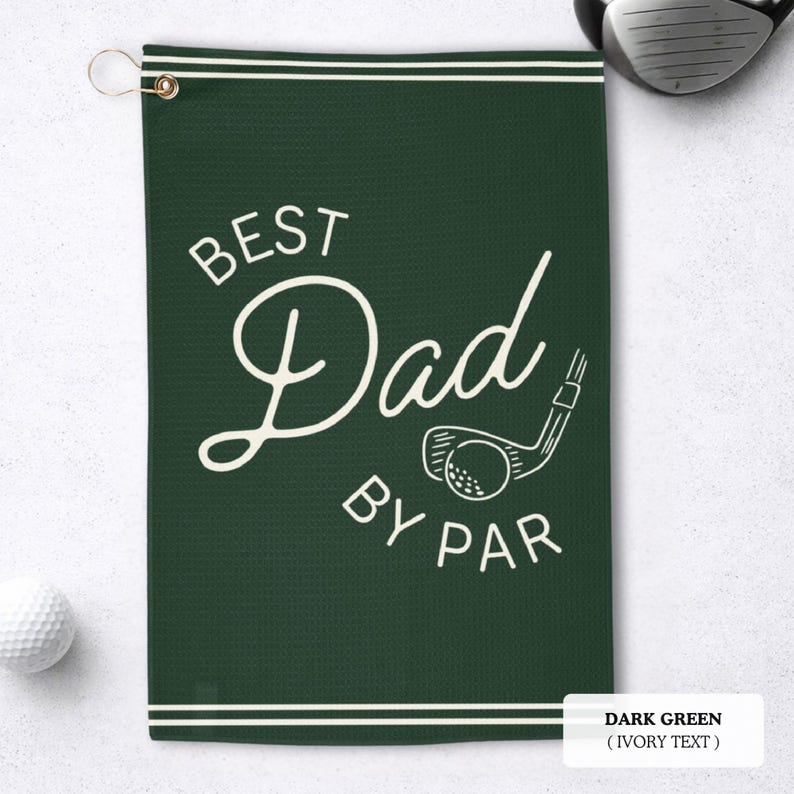 May include: Dark green golf towel with the text "BEST Dad BY PAR" in ivory script. A golf club and ball graphic is also featured. The towel has a metal grommet and a white border.