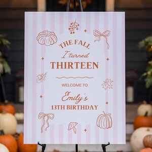 Puede incluir: Un letrero rectangular con rayas verticales de color rosa claro y blanco, con dibujos lineales naranjas de calabazas, lazos, hojas y setas. El texto dice: THE FALL I turned THIRTEEN WELCOME TO Emily's 13TH BIRTHDAY, decorado con pequeñas estrellas.