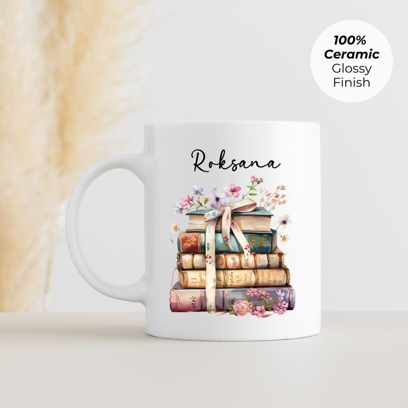 Puede incluir: Taza de cer&aacute;mica blanca con una pila de libros adornada con flores y una cinta. El nombre "Roksana" est&aacute; escrito en cursiva encima de los libros. La taza tiene un acabado brillante y el texto "100% Ceramic Glossy Finish".