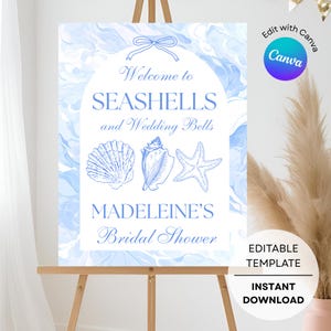 May include: A blue and white sign on an easel with the text "Welcome to Seashells and Wedding Bells" and "Madeleine's Bridal Shower." The sign features illustrations of seashells and a starfish. The words "Editable Template" and "Instant Download" are also visible.