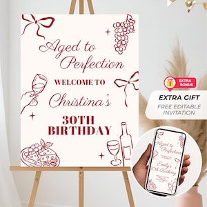 May include: Aged to Perfection birthday sign with wine-themed illustrations and text. The sign says "Welcome to Christina's 30th Birthday." A phone displays a similar design for Emily's 50th birthday. Includes a bonus gift.