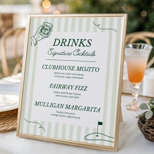 May include: A framed sign with a gold border displays a list of "DRINKS Signature Cocktails." The sign features a green and white striped background and includes the names and ingredients of three cocktails: Clubhouse Mojito, Fairway Fizz, and Mulligan Margarita. A golf-themed illustration is at the bottom.