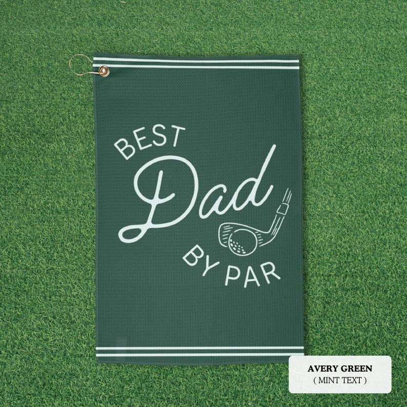 May include: Avery green golf towel with the text "BEST Dad BY PAR" in white script and a golf club graphic. The towel has a white border and a metal grommet for hanging.