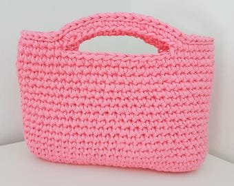 Könnte beinhalten: Eine leuchtend pinke Handtasche aus dickem, gehäkeltem Garn. Die Tasche hat einen rechteckigen Körper mit einem durchgehend gleichmäßigen, strukturierten Maschenbild und zwei integrierten, abgerundeten Griffen an der Oberseite.