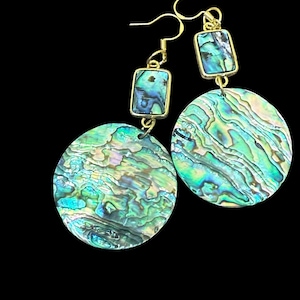 May include: A pair of gold-toned earrings with iridescent abalone shell accents. Each earring features a rectangular top piece and a large, round bottom piece. The abalone shell displays shades of green, blue, and purple. The earrings hang from gold-colored hooks.