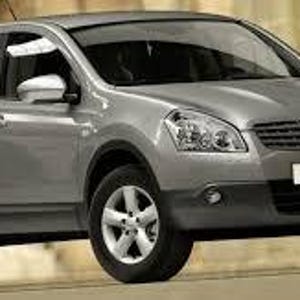 Pode incluir: Um SUV Nissan Qashqai prateado com pneus pretos e um para-choques inferior preto. O veículo tem uma proeminente grelha dianteira e faróis. A palavra "Qashqai" é exibida na frente.