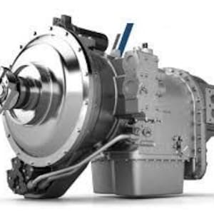 Puede incluir: Primer plano de un componente de máquina industrial plateado. El componente tiene una sección grande y circular a la izquierda y una sección rectangular a la derecha. Cuenta con varias tuberías, pernos y detalles mecánicos, sobre un fondo blanco.