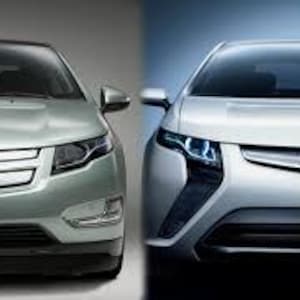 Può includere: Due auto elettriche argentate sono mostrate fianco a fianco. L'auto a sinistra ha un emblema Chevrolet, mentre l'auto a destra ha un emblema Opel. Entrambe le auto hanno un design moderno con fari e griglie prominenti.